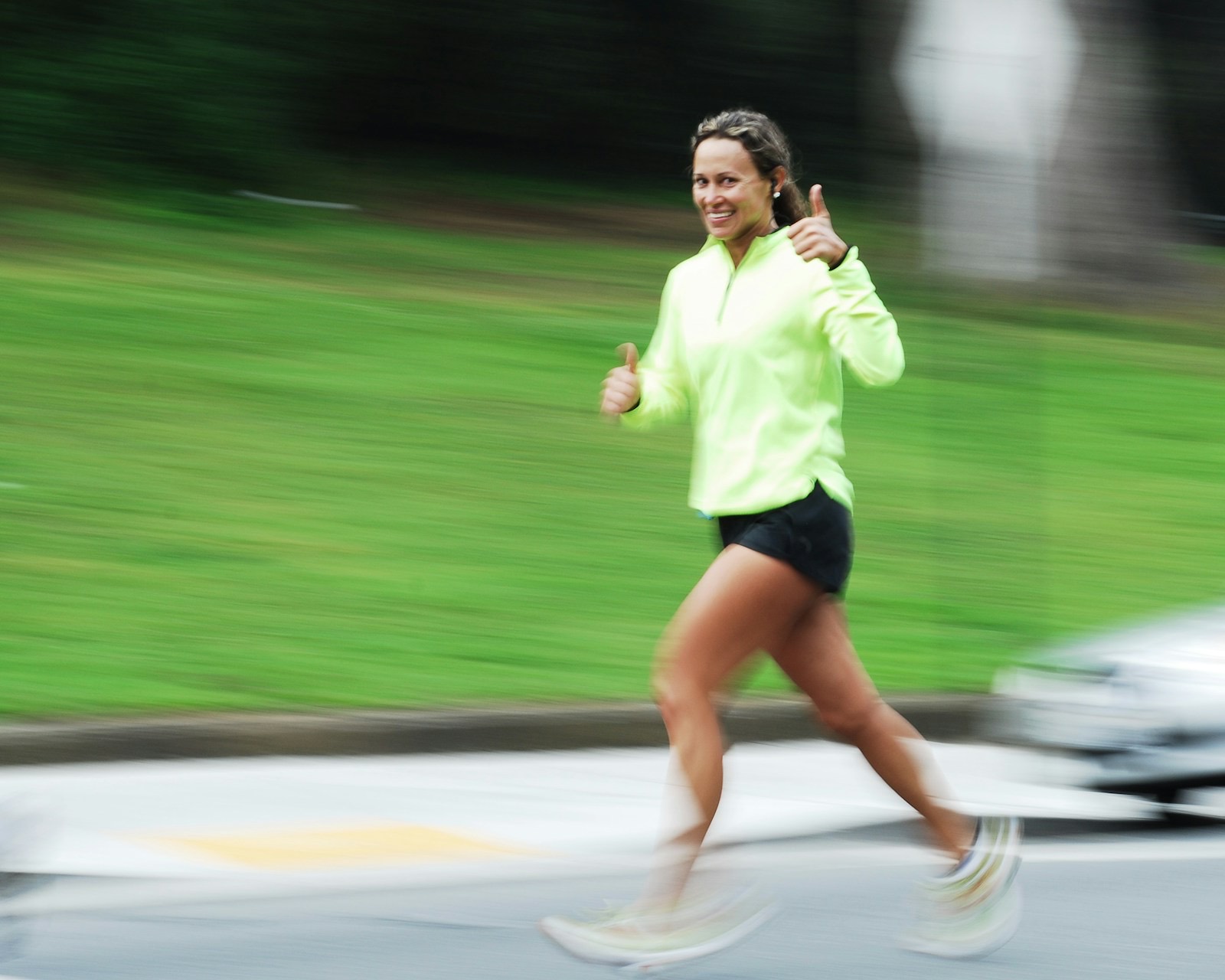 A woman runs through a park and gives a thumbs up